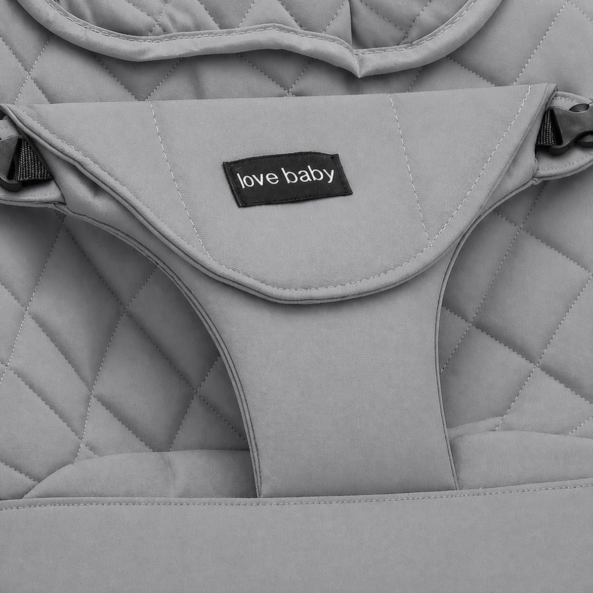 Close-up of a light gray quilted baby bouncer or seat pad with a black fabric label reading 'love baby' in white text.
